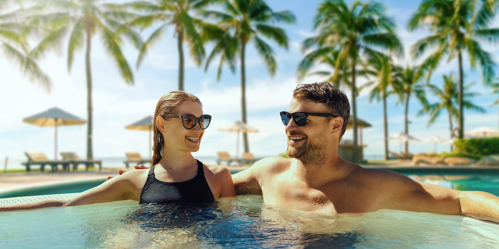 Reiseberatung für Cluburlaub, Paar mit Sonnenbrillen entspannt im Pool während ihres Cluburlaubs, Palmen und Sonnenliegen im Hintergrund